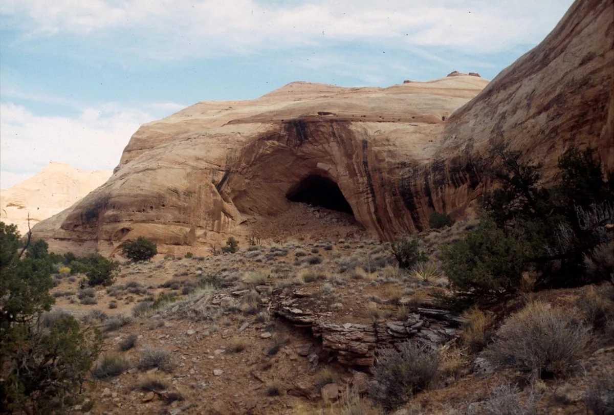 Islamic Stories A large cave opening in a curved sandstone cliff above a rocky desert slope with shrubs